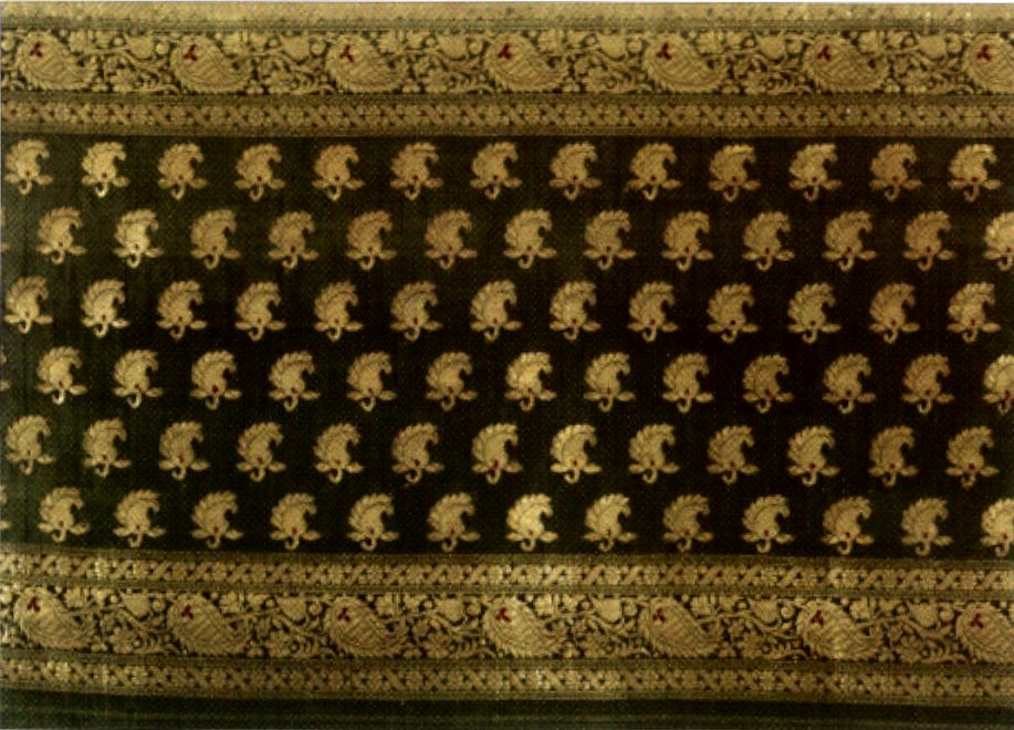 Banarasi Silk | The India A richly patterned Banarasi silk fabric showcases intricate gold floral designs and brocade weaving.