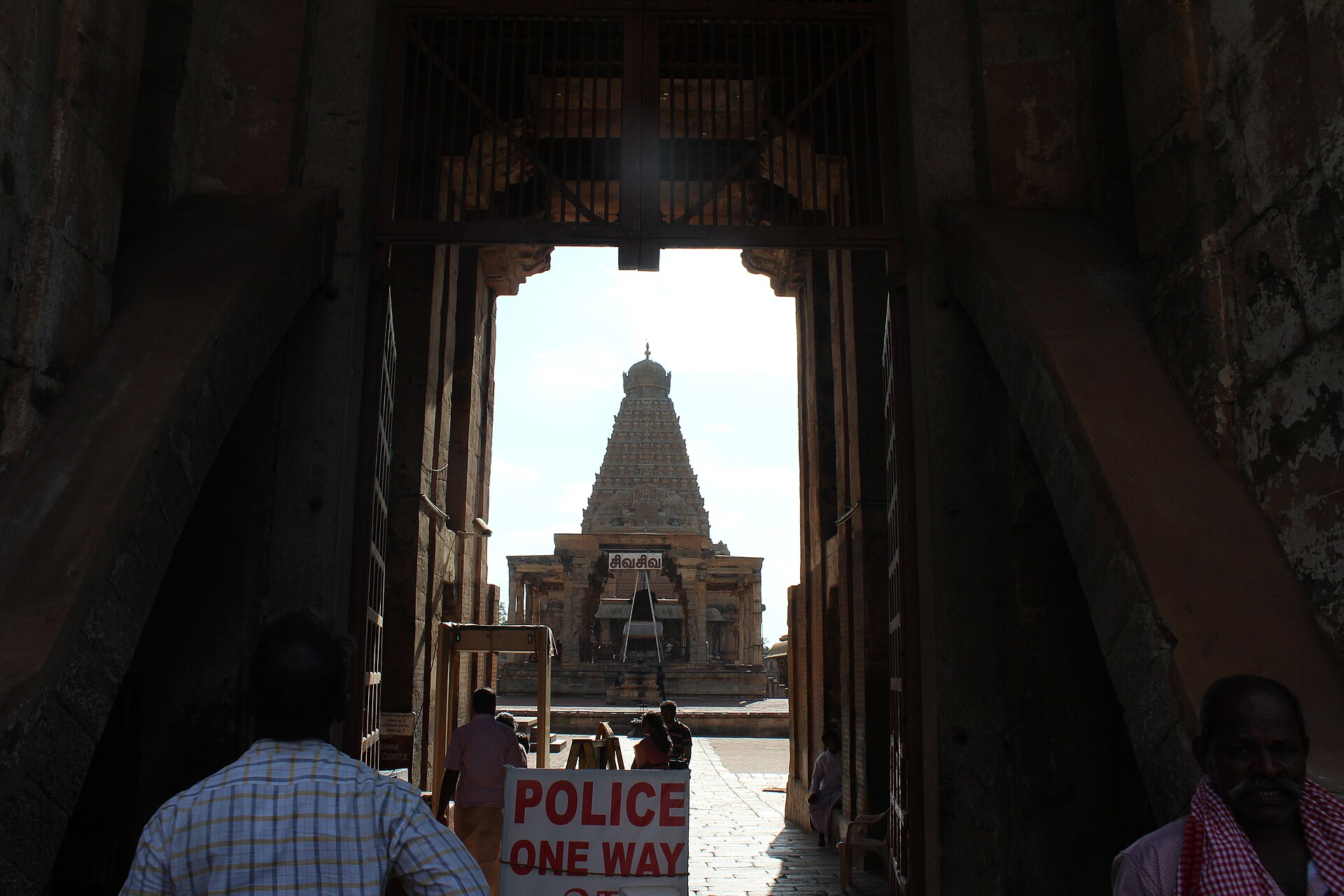 Dravidian Temple | The India A temple gopuram is framed by a stone gateway with people and signage, showcasing Indian architecture.