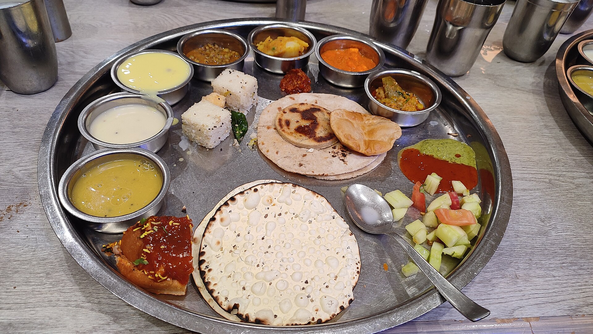 Gujarati Thali | The India A large metal thali displays a variety of Indian dishes and breads, showcasing delicious indian cuisine.