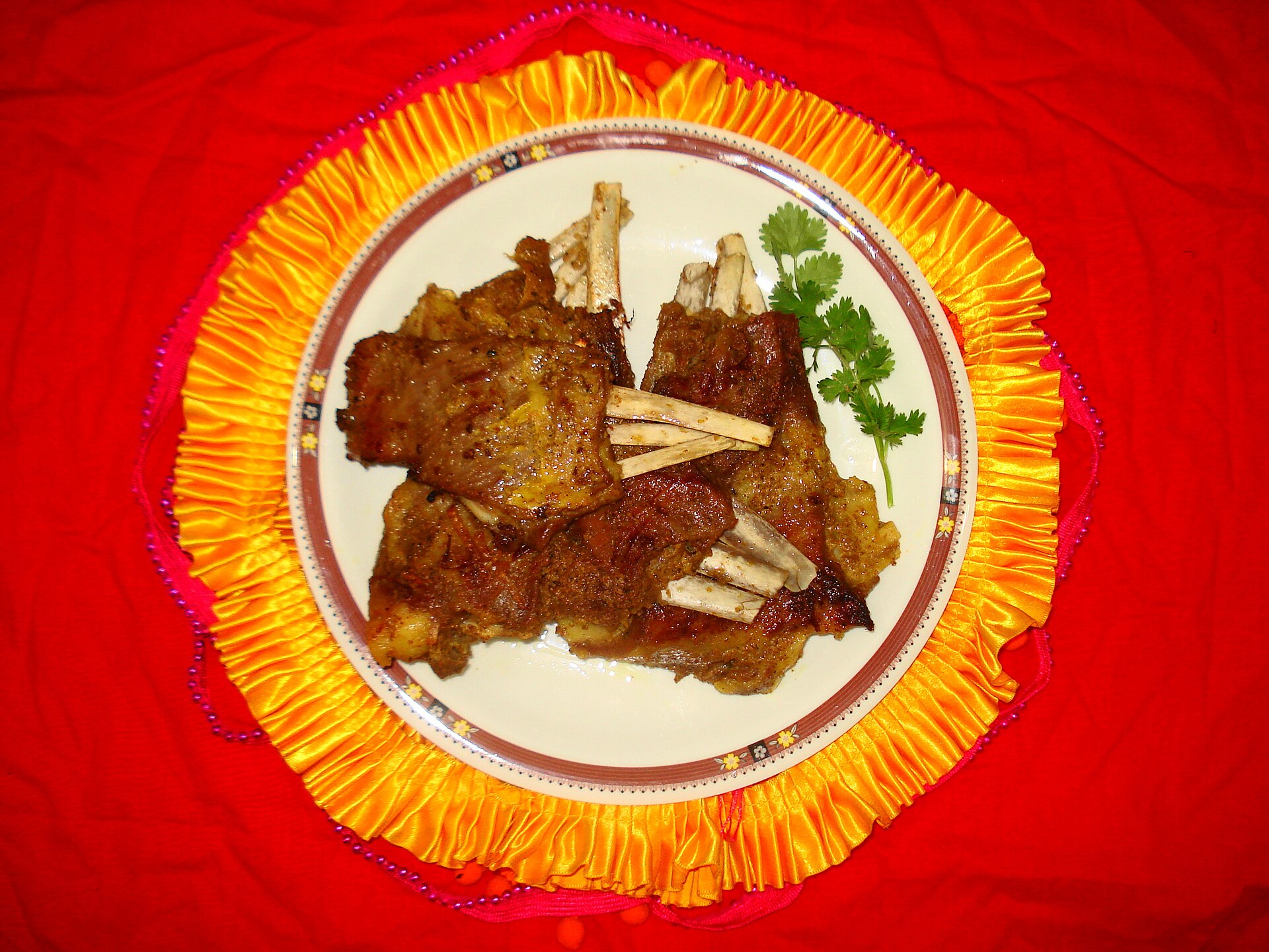 Kashmiri Wazwan Ceremony | The India A plate of Tabak Maaz, lamb chops garnished with cilantro, showcases traditional indian cuisine.