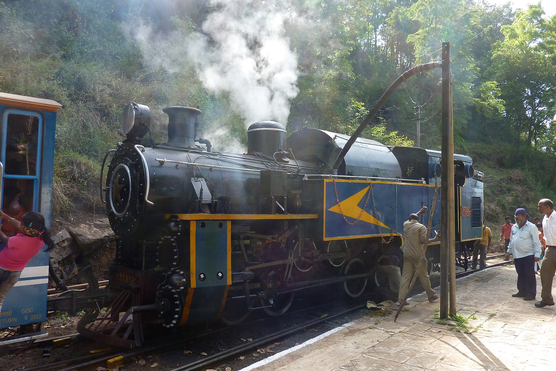 Nilgiri Mountain Railway | The India A steam locomotive on the Nilgiri Mountain Railway tracks with people nearby, showcasing travel in India.